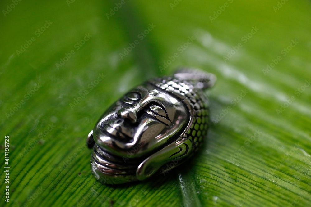Silver Buddha medallion on a green leave.  Kep. Cambodia.  25.02.2017