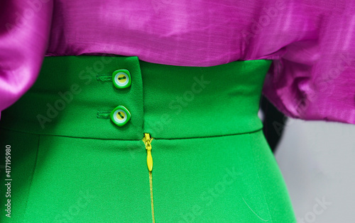 A bright green skirt with dramatic buttons and a lilac silk blouse. Close-up details. Contrasting designs. Textile backgrounds.
