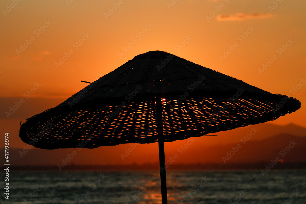 sunset from behind the straw umbrella on the beach
