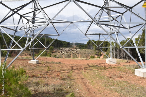 Fototapeta Light tower in the mountains with reforested pine forest and firebreak with high voltage line