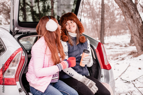 two girls had a winter picnic together. Mom and student daughter are sitting in the car. Mother and daughter sit in the trunk of a car and drink tea from a thermos 
