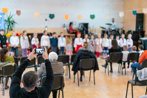 Parents at the performance of children in kindergarten or school. Children on stage. Many parents are watching the kids performance in the hall during Chistmas holiday, blur