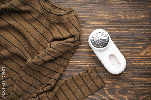 Фотография Modern fabric shaver and clothes on wooden background. Flat lay.