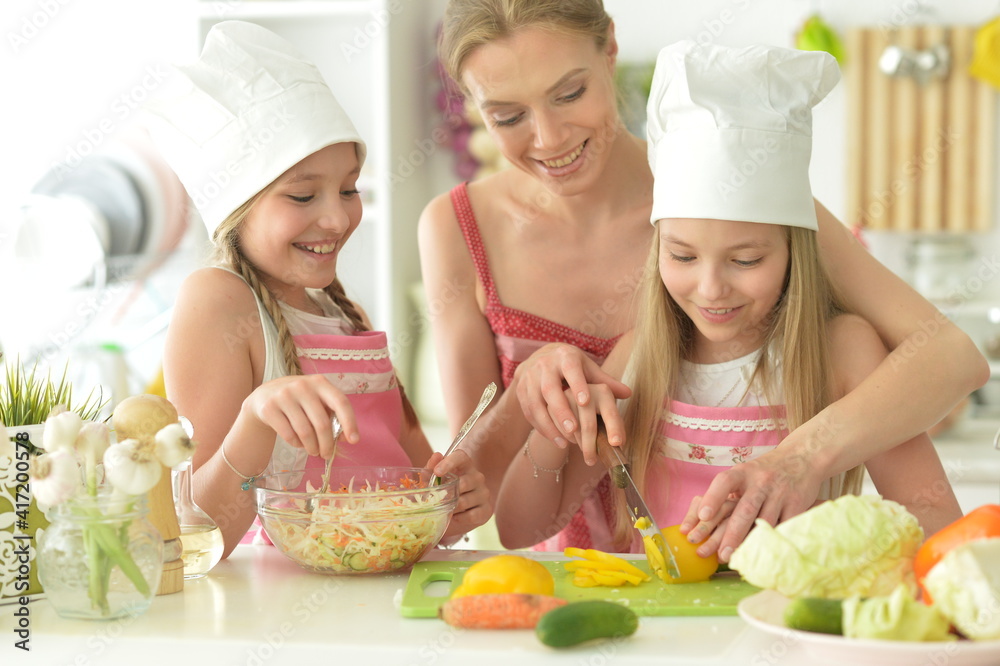Cute girls with mother preparing delicious fresh salad in kitchen Cute girls with mother preparing delicious fresh salad in kitchen