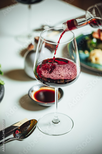 Selective focus shot of pouring red wine into the glass on a white table, dinner table at restaurant