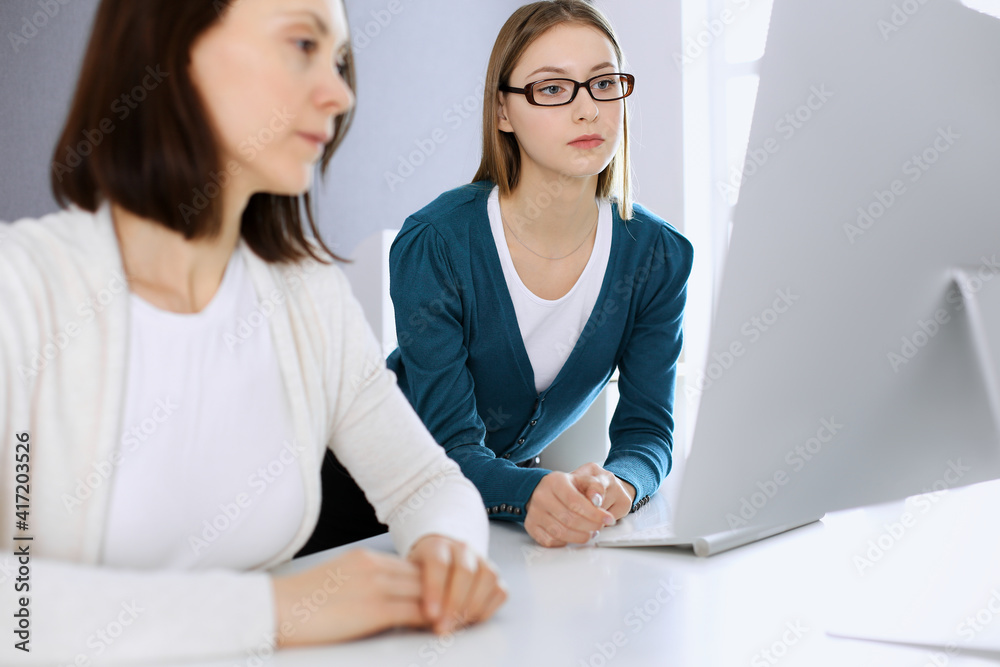 Businesswoman giving presentation to her female colleague while they sitting at the desk with computer. Group of business people working in office. Teamwork concept Businesswoman giving presentation to her female colleague while they sitting at the desk with computer. Group of business people working in office. Teamwork concept