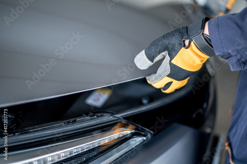 Obraz na plátně Male auto mechanic hand wearing yellow glove opening car bonnet hood