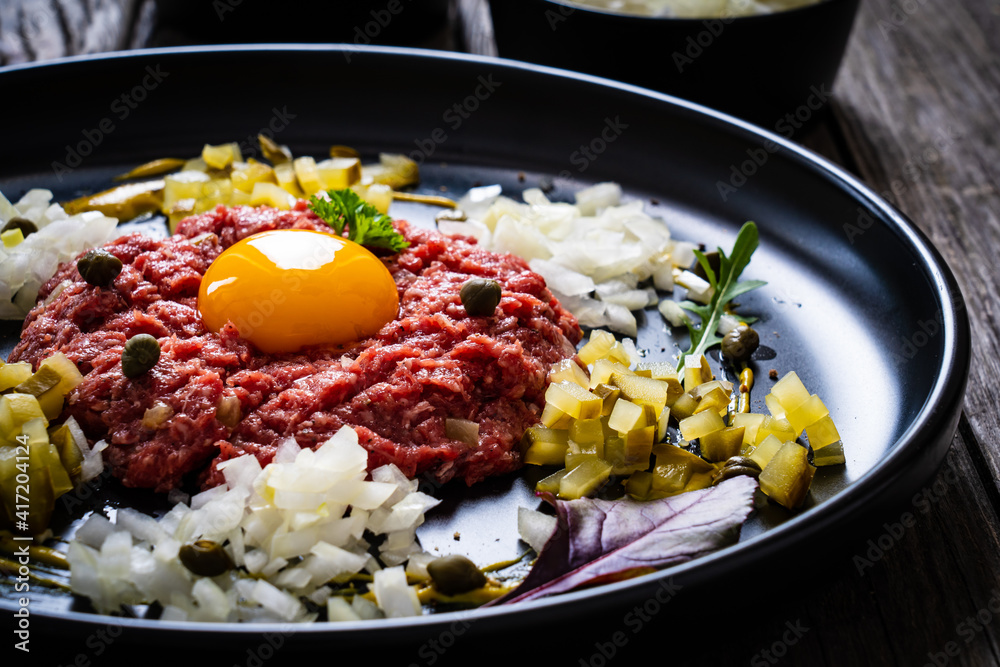 Beef tartare steak with onion, capers and pickled cucumbers on wooden table