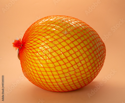 Mature pomelo in a net on a peach background