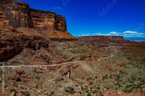 Dirt road at the bottom of the canyon among the layered geological formations of red rocks.