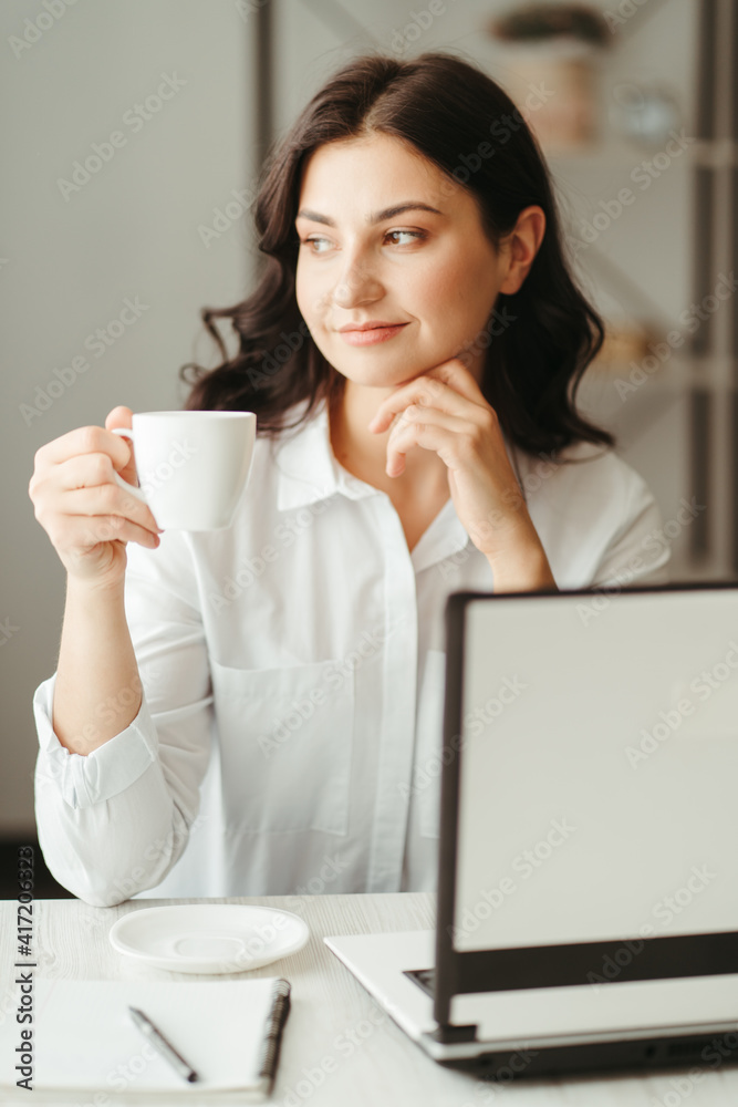 Woman enjoying coffee while working, sitting at the desk with laptop in her home office. Remote work, freelance, using laptop computer or net-book Woman enjoying coffee while working, sitting at the desk with laptop in her home office. Remote work, freelance, using laptop computer or net-book