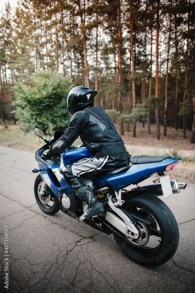 Rear view of motorcycle driver driving in helmet with blurred forest background