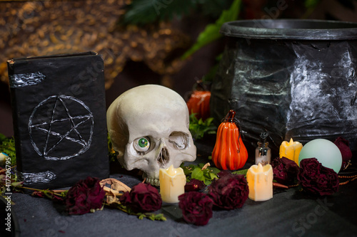 Black book with pentagram, skull and cauldron on the table with witchcraft ingredients. Halloween witch altar concept. photo