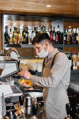 A masked barista prepares delicious coffee at the bar in a cafe. The work of restaurants and cafes during the pandemic.