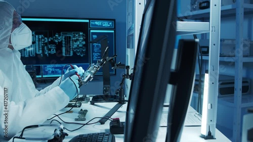 Microelectronics engineer works in a modern scientific laboratory on computing systems and microprocessors. Electronic factory worker is testing the motherboard and coding the firmware.
