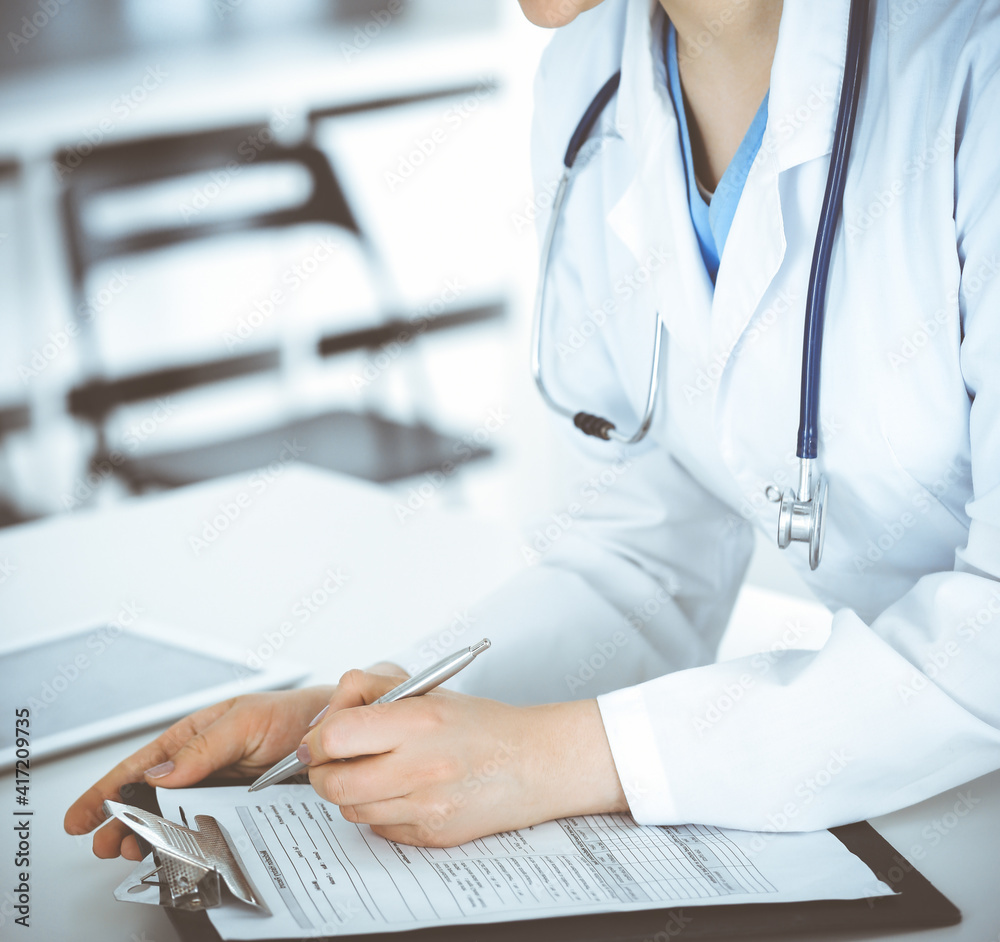 Unknown woman-doctor or internal student filling up medical documents while standing in clinic reception desk. Data in medicine Unknown woman-doctor or internal student filling up medical documents while standing in clinic reception desk. Data in medicine