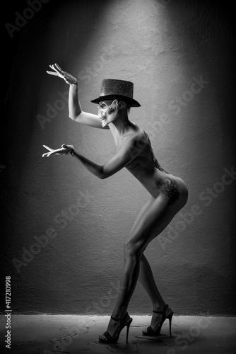 Beautiful, naked girl with a tattoo in white gloves and a skull mask with rhinestones and a top hat