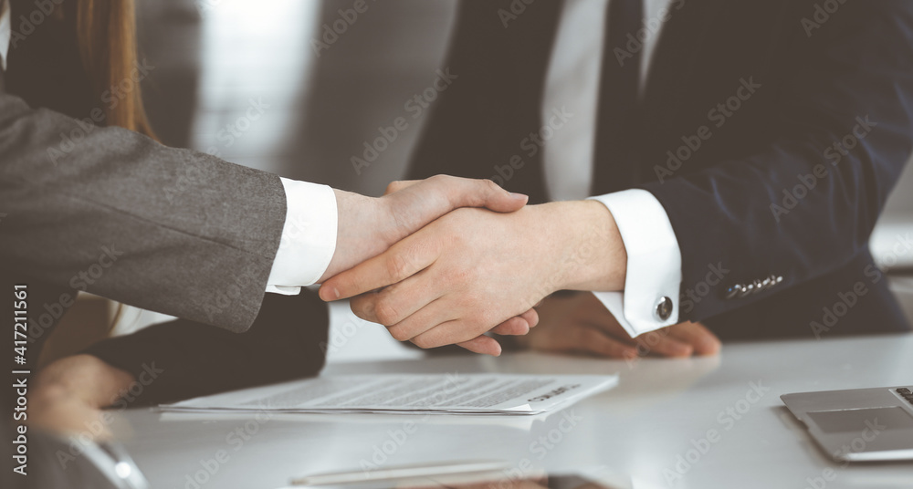 Unknown businessman shaking hands with his colleague or partner above the glass desk in modern office, close-up. Business people group at meeting Unknown businessman shaking hands with his colleague or partner above the glass desk in modern office, close-up. Business people group at meeting