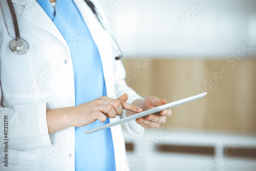 Unknown woman-doctor standing in clinic and using tablet pc, close-up. Data in medicine and healthcare © Iryna