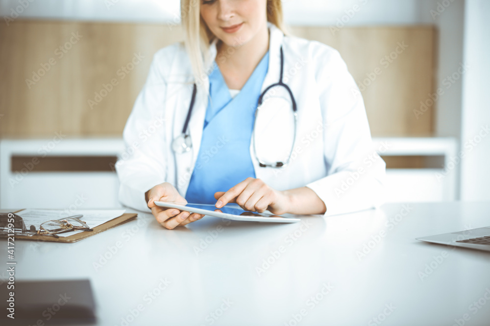 Unknown woman-doctor standing in clinic and using tablet pc, close-up. Data and best service in medicine and healthcare Unknown woman-doctor standing in clinic and using tablet pc, close-up. Data and best service in medicine and healthcare