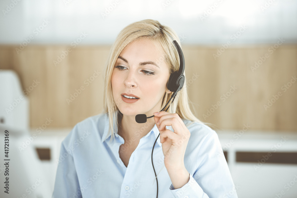 Blonde business woman sitting and communicated by headset in call center office. Concept of telesales business or home office occupation Blonde business woman sitting and communicated by headset in call center office. Concept of telesales business or home office occupation