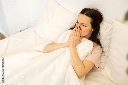 beautiful young woman lies on bed under the covers with a cold 