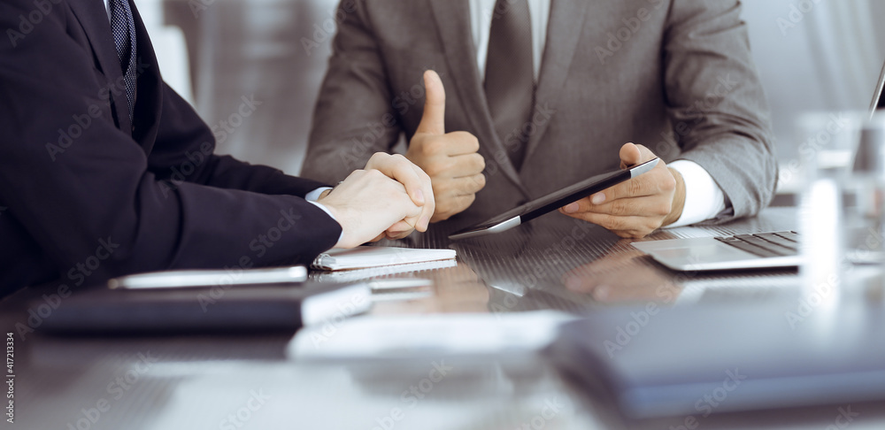 Unknown businessman using tablet computer and working together with his colleague while sits at the glass desk in modern office. Teamwork and partnership concept Unknown businessman using tablet computer and working together with his colleague while sits at the glass desk in modern office. Teamwork and partnership concept
