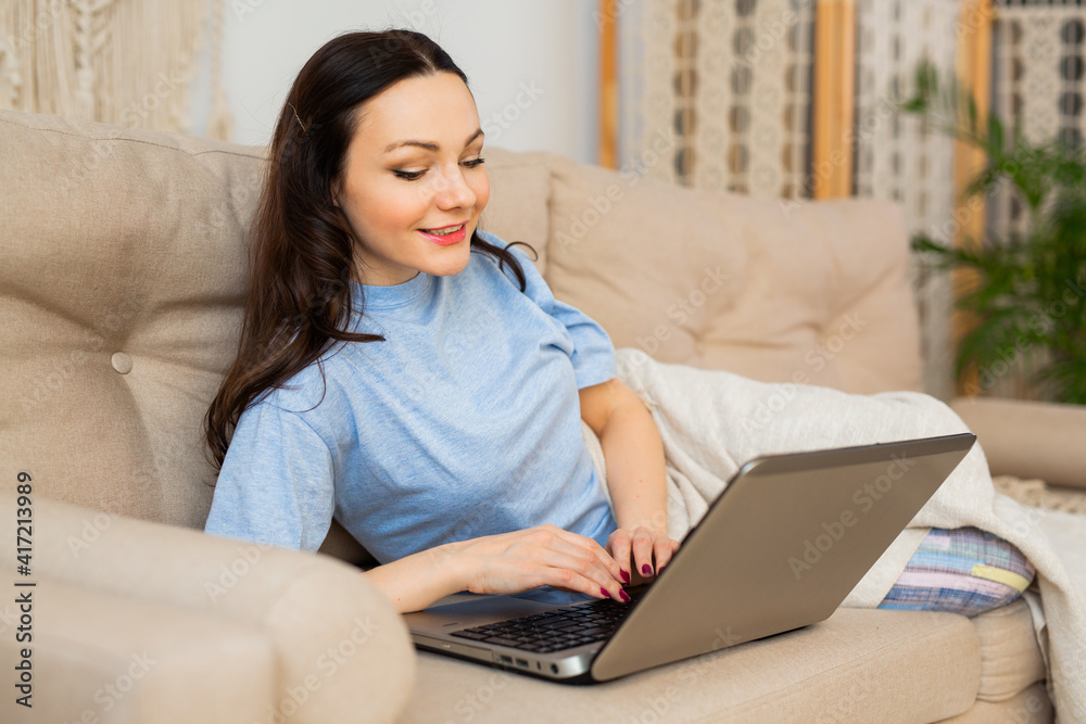beautiful young woman in pajamas lies at home on the couch with a laptop beautiful young woman in pajamas lies at home on the couch with a laptop
