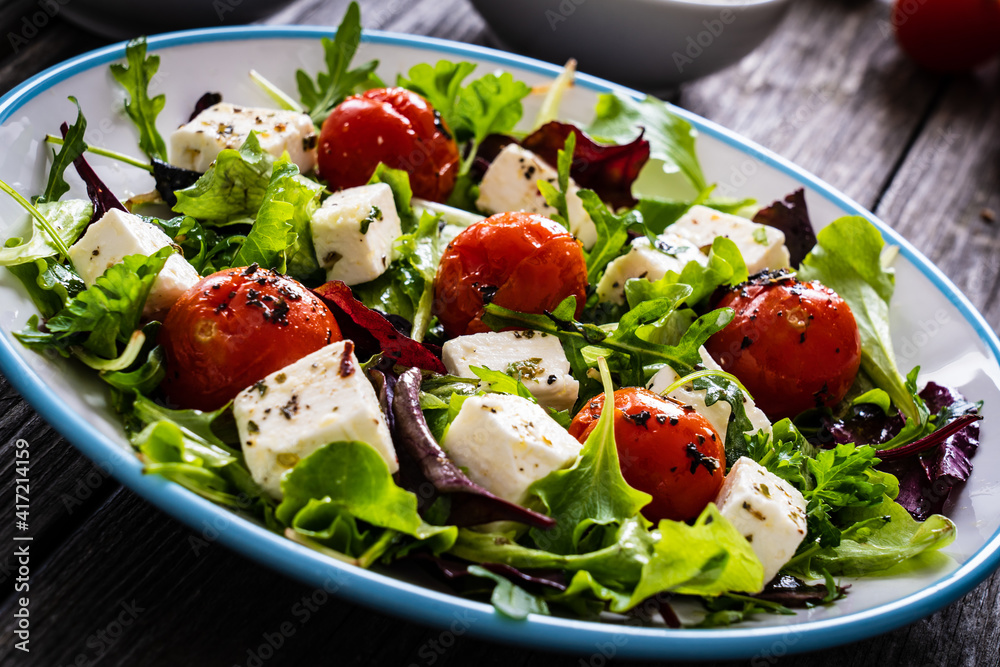 Fresh vegetable salad with feta cheese, tomatoes, arugula, lettuce and roast tomatoes on wooden table
Fresh vegetable salad with feta cheese, tomatoes, arugula, lettuce and roast tomatoes on wooden table