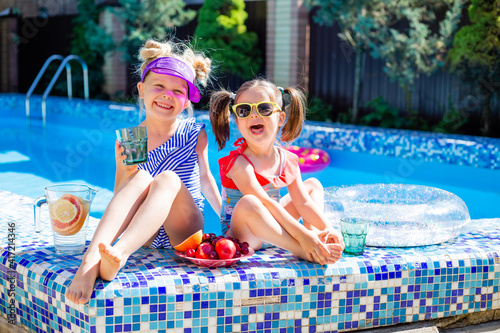 two little girls in a pool with fruit and refreshing cocktails, wearing glasses and swimsuits. children's summer vacation