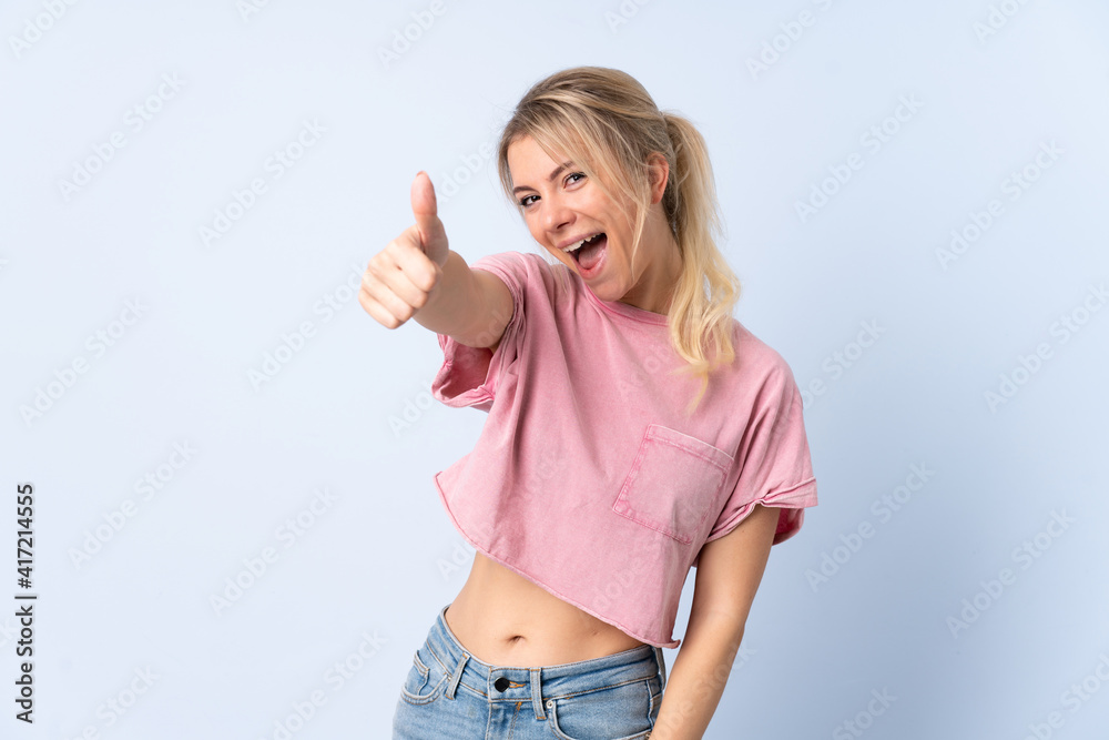 Blonde woman over isolated blue background with thumbs up because something good has happened Blonde woman over isolated blue background with thumbs up because something good has happened