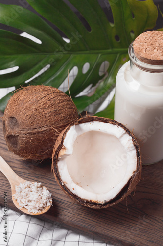 Glass bottle with milk or yogurt on dark wooden board with coconuts and flakes. Tropical composition