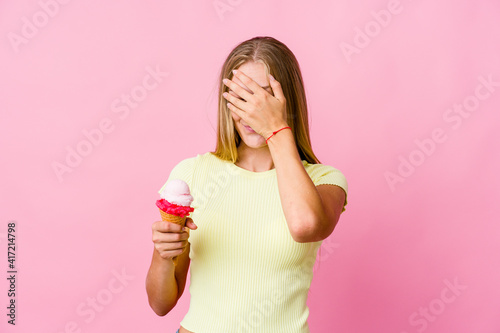 Young russian woman eating an ice cream isolated covers eyes with hands, smiles broadly waiting for a surprise.