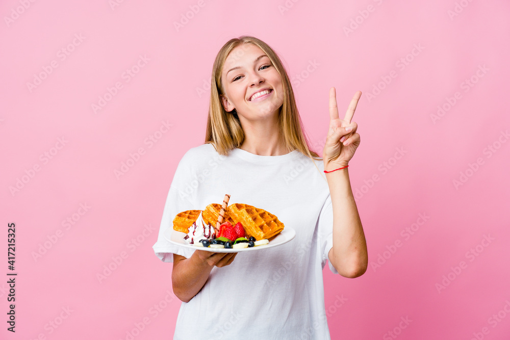 Young russian woman eating a waffle isolated showing number two with fingers. Young russian woman eating a waffle isolated showing number two with fingers.