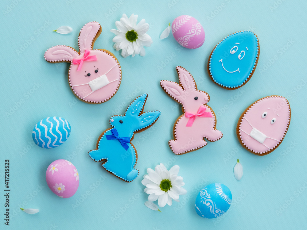 Covid-19 Easter. Festive pattern. Spring holiday ornament. Sweet pastry composition. Pink blue gingerbread biscuit bunny egg with face in mask design white flowers isolated on light background.