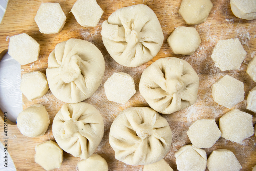 Handmade khinkali dumplings and ravioli are beautifully arranged in rows on a cutting board and sprinkled with flour. Close-up, macro.