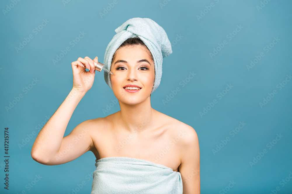 Closeup studio portrait with young woman in bath towel on head isolated on copy space applying oil serum from pipette. Natural organic cosmetic product for facial skincare and skin regeneration. Closeup studio portrait with young woman in bath towel on head isolated on copy space applying oil serum from pipette. Natural organic cosmetic product for facial skincare and skin regeneration.