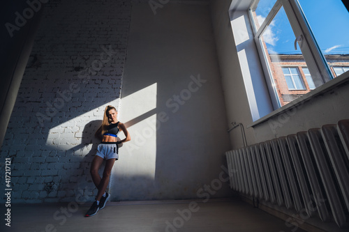 Fototapeta Naklejka Na Ścianę i Meble -  Beautiful contrasting portrait with the play of light and shadow of a young and fit girl in a loft interior with a white brick wall