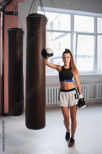 Beautiful kickboxing woman training with bag in fitness studio. © romankosolapov