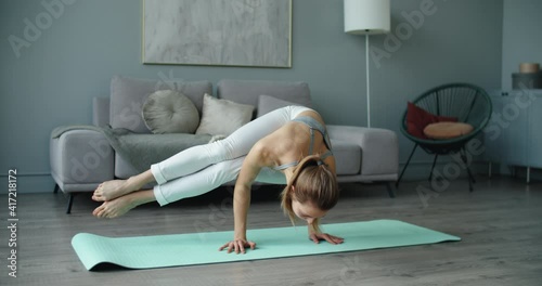 Sports happy beautiful young woman practicing yoga, doing arm stand, asymmetrical arm balance, working out wearing white sportswear, home, full length. High quality 4k footage photo