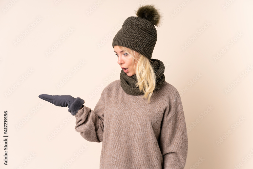Young woman with winter hat over isolated background holding copyspace imaginary on the palm Young woman with winter hat over isolated background holding copyspace imaginary on the palm
