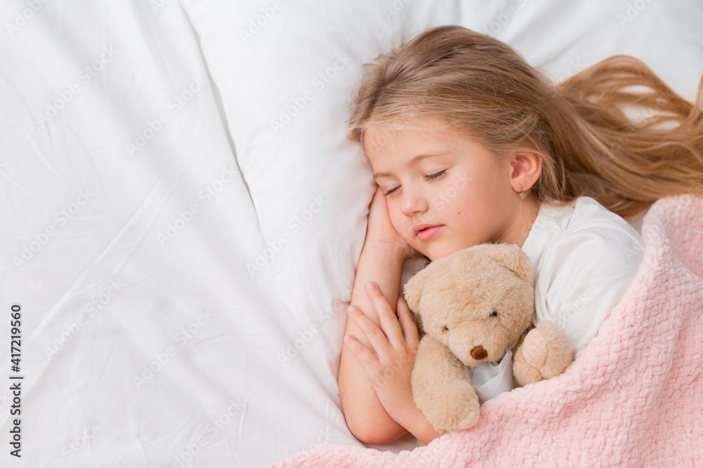 little blonde girl sleeping in bed hugging a teddy bear under a pink knitted blanket, space for text little blonde girl sleeping in bed hugging a teddy bear under a pink knitted blanket, space for text