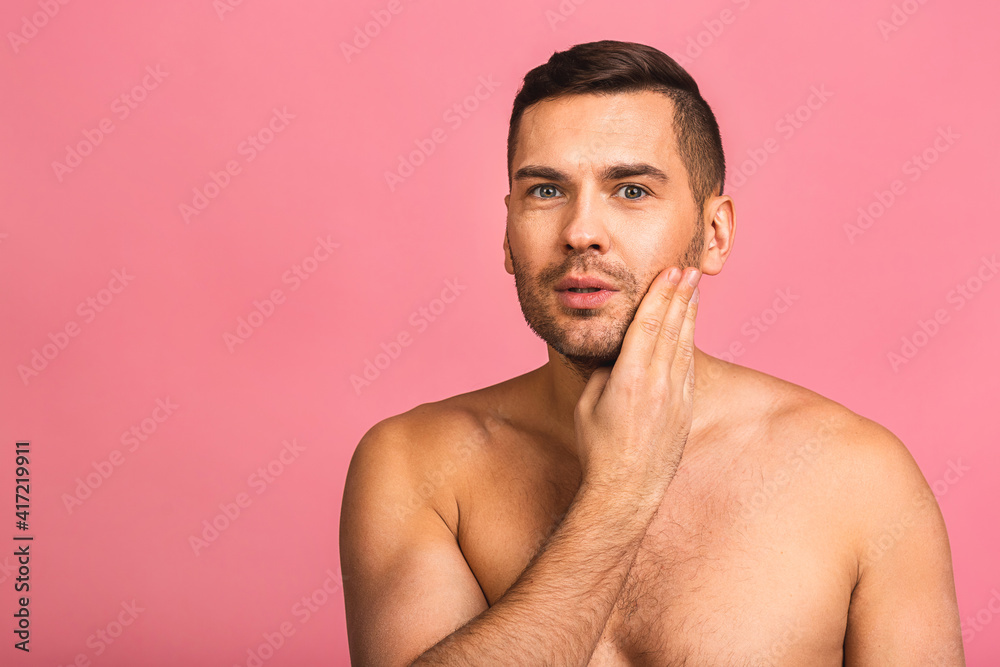 Fototapeta premium Photo of smiling young beautiful man standing isolated over pink wall background naked. Man's skincare concept in a bathroom.