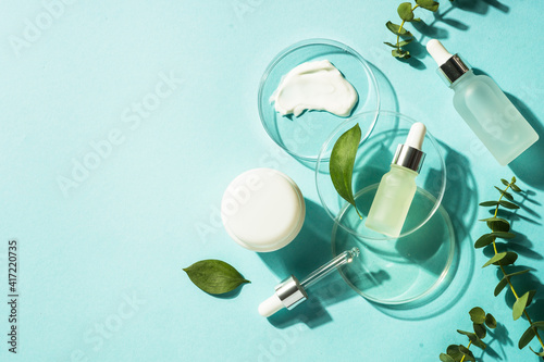 Cosmetic laboratory concept . Glass petri dish with cosmetic products and serum bottles at blue background. Flat lay image with copy space.