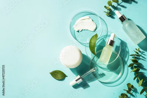 Obraz Cosmetic laboratory concept . Glass petri dish with cosmetic products and serum bottles at blue background. Flat lay image with copy space.