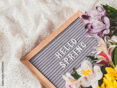 Letter board with season greeting HELLO SPRING on laces white textile background with fresh alstroemeria flowers.