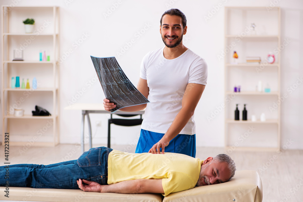 Obraz premium Old male patient visiting young male doctor chiropractor