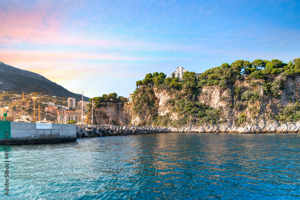 The rugged steep coastline of Monte Carlo, Monaco, with the Monaco Cathedral overlooking the Fontvieille Harbor and Mediterranean Sea near sunset.