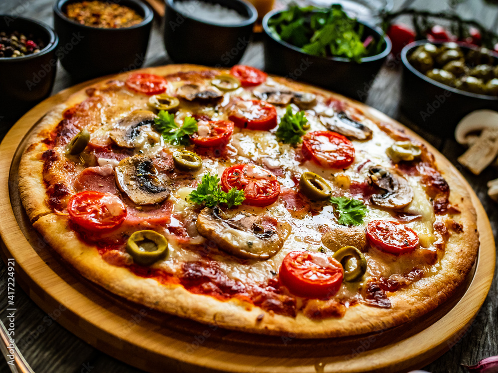 Pizza with champignons, ham, tomatoes, olives, parmesan and mozzarella  on wooden background
