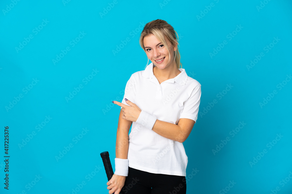 Young Russian woman isolated on blue background playing tennis and pointing to the lateral Young Russian woman isolated on blue background playing tennis and pointing to the lateral
